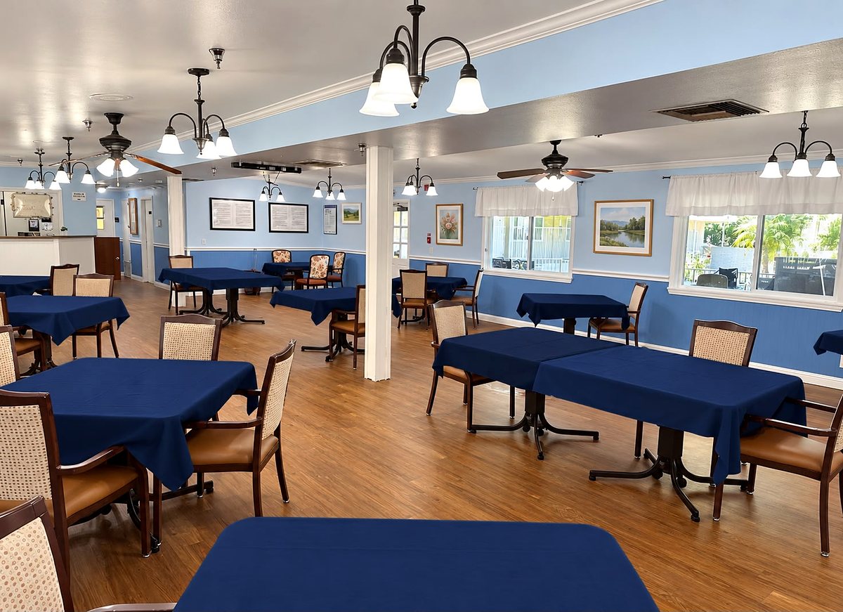 The bright dining room at Paradise Gardens Manor, with tables in new navy-blue tablecloths, chandeliers and garden-view windows