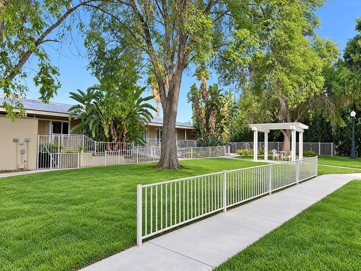 Green lawn with a walkway, white fencing and a gazebo under tall shade trees